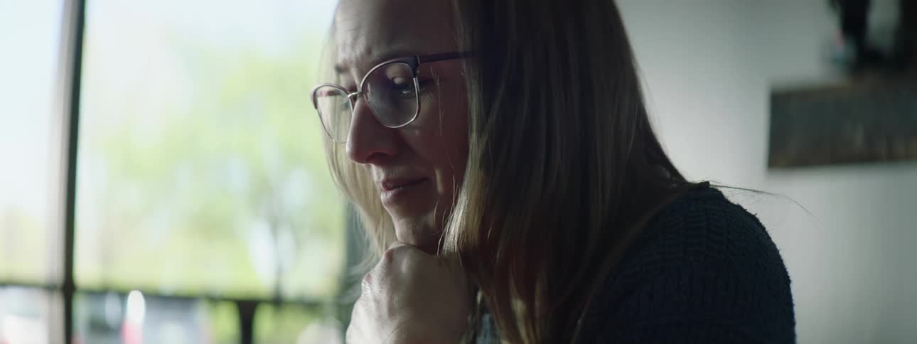 Blonde woman with glasses and blue sweater uses laptop in room