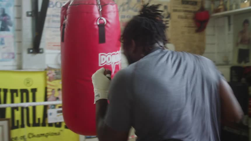 A large man with his hands taped up repeatedly hits a punching bag
