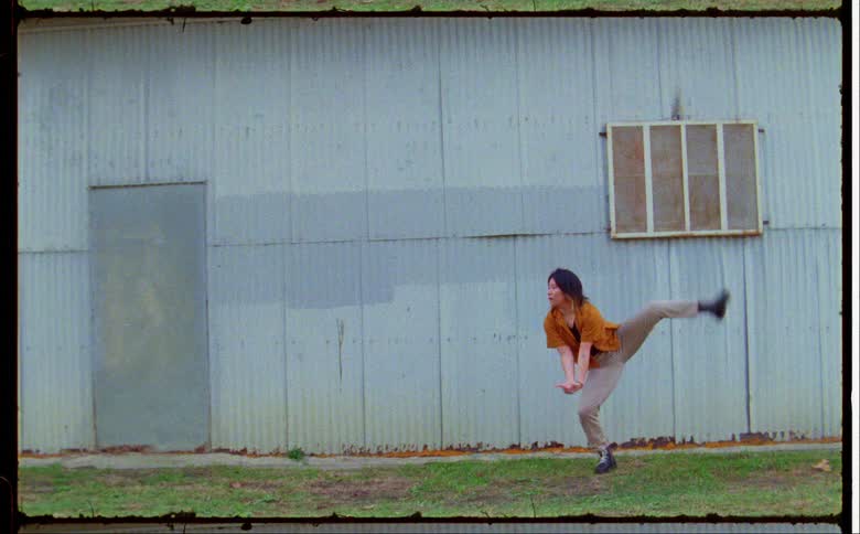 A woman wearing an orange overshirt dancing in front of a blue building