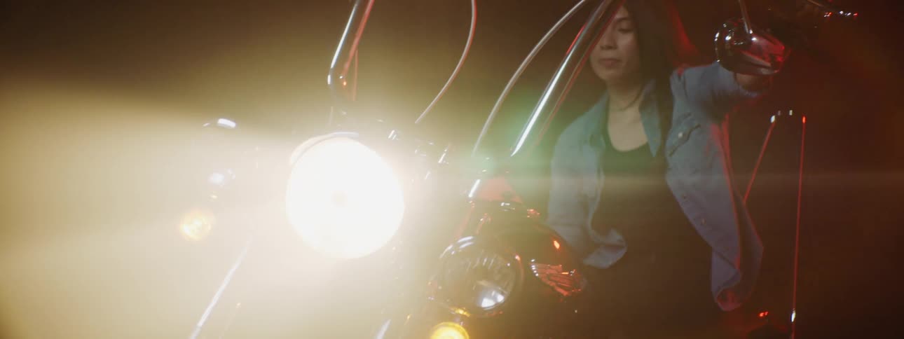 A woman is getting on a motorcycle during the night