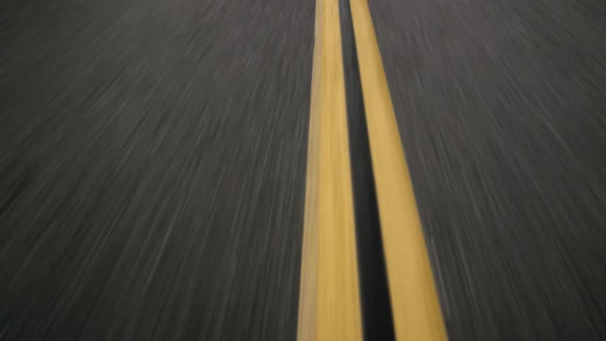 An up close drone view of a paved road with yellow stripes down the middle