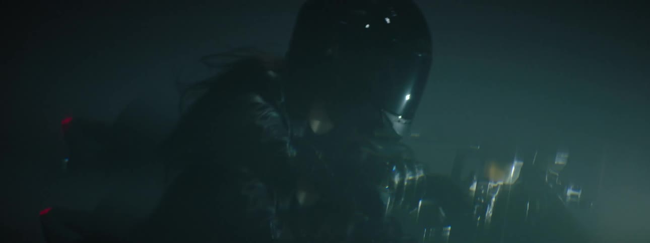 A woman wearing all black driving a black motorcycle at night