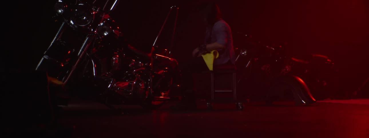 A person walking over to a motorcycle with a rag sitting down on a stool and then throwing the rag on the ground standing up and walking away