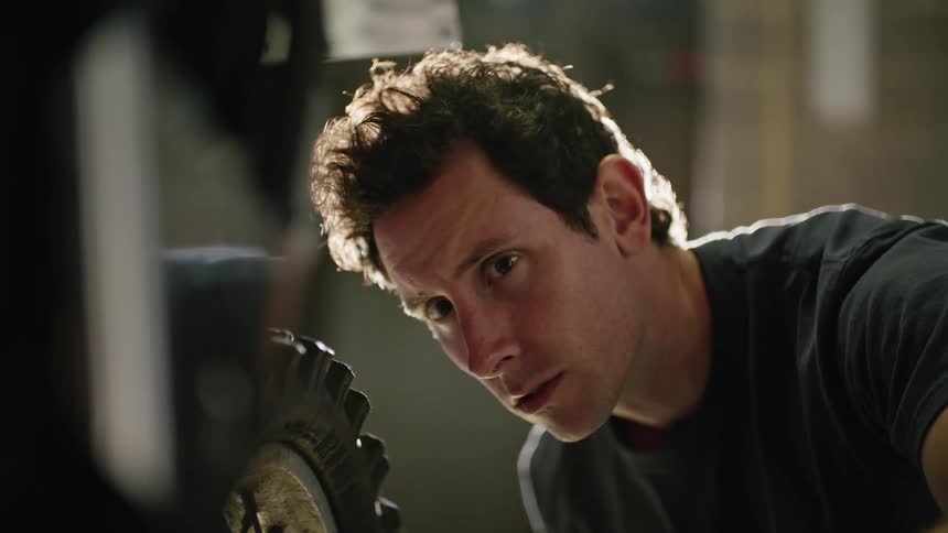Man manually turns tire while examining motorcycle