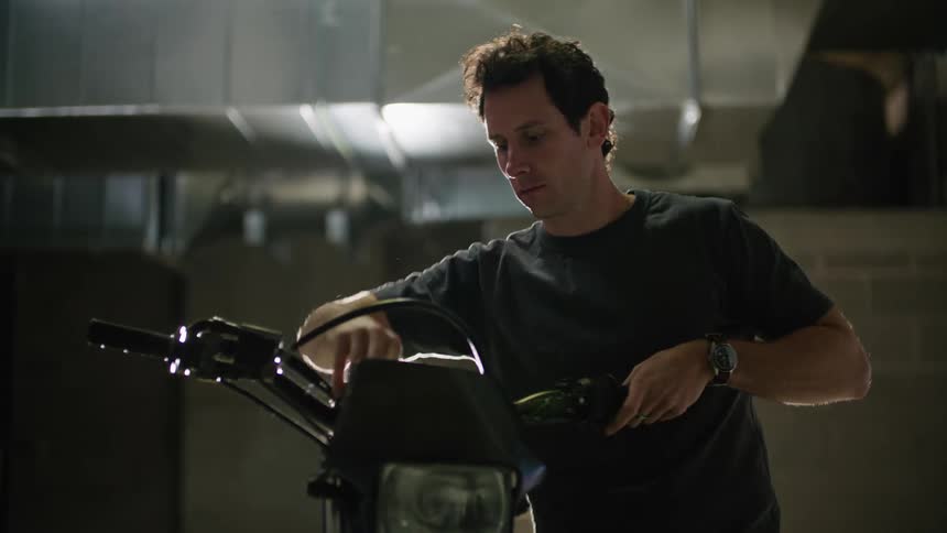 Man with black t shirt and wristwatch fixes motorcycle in building