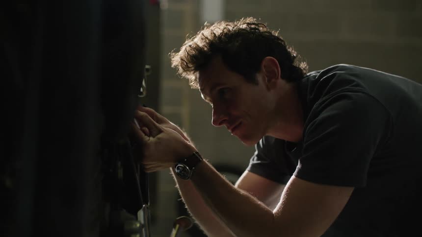 A man knelt down screwing something into a part using tools
