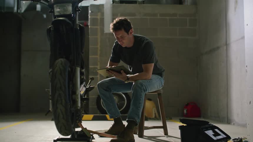 A man consults a manual while fixing his motorcycle