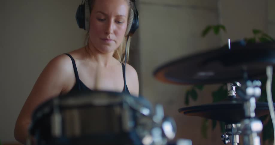 A young woman wearing headphones is playing a set of drums