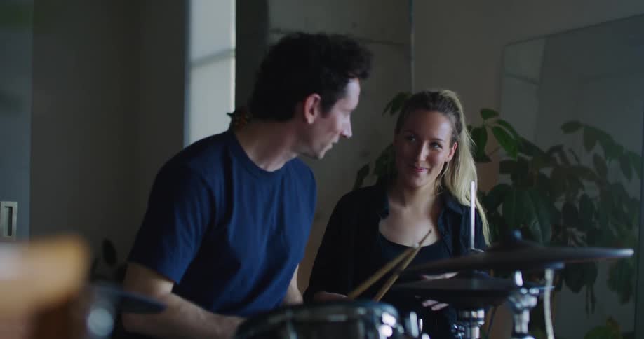 Man in blue shirt plays drums next to blonde woman with ponytail and black shirt