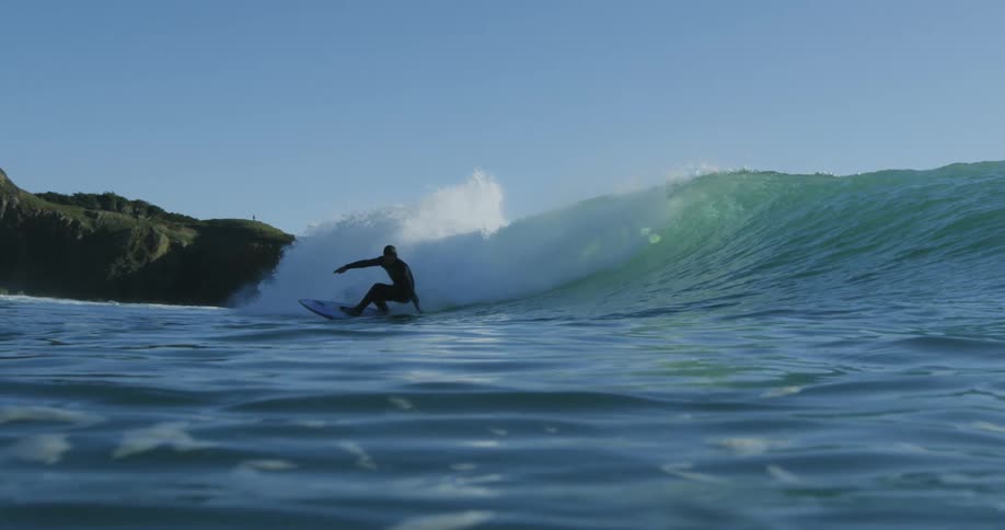 Surfer rides wave rolling toward beach under a clear sky