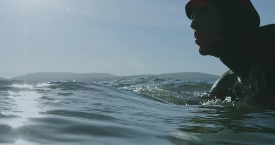 A close up of a man on a surf board hand paddling through the water