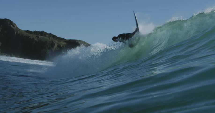 Water splashes as a surfer rides a big wave and the view moves to underwater