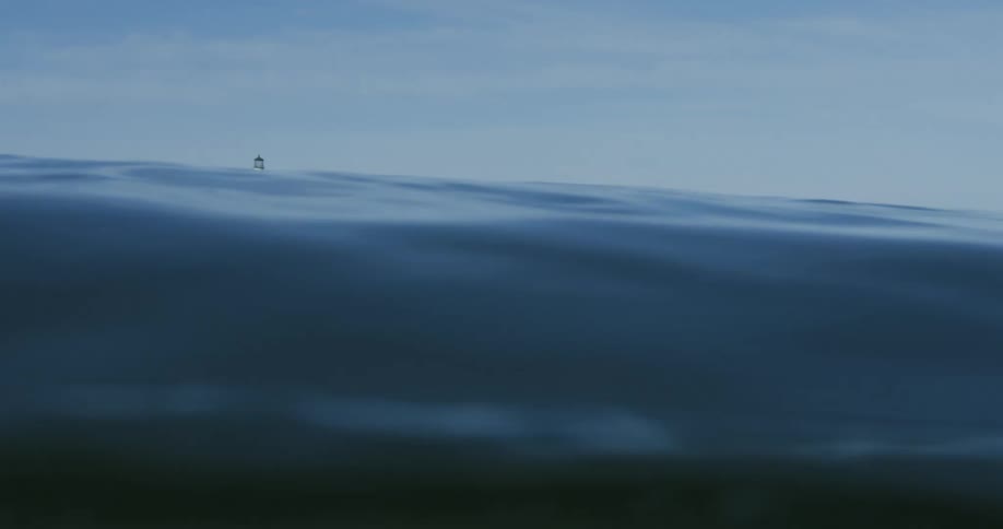 Waves in the water rising and falling along a coastline with a lighthouse on the land