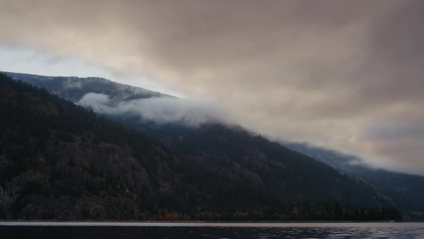 Clouds move low over a mountain along the coast under a hazy sky