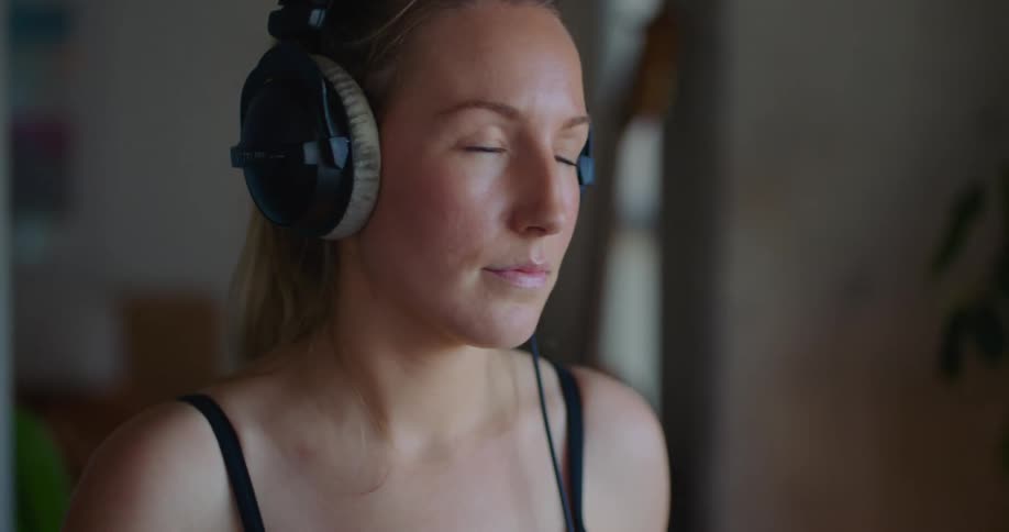A close up of a woman wearing headphones shaking her head as she drums on a drumset