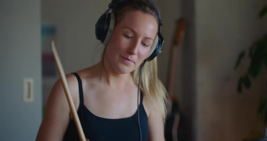 A woman wears headphones while playing the drums