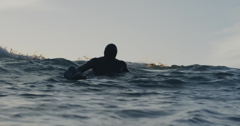 A person in a wet suit paddling out on the ocean on a surf board towards the waves