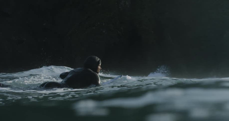 Man in wetsuit swims on surfboard in water