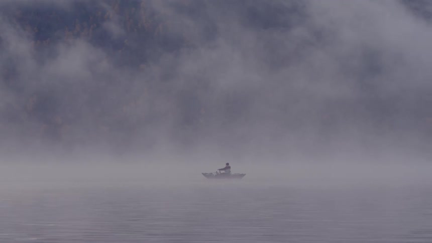 A man rows a boat across the water through thick fog