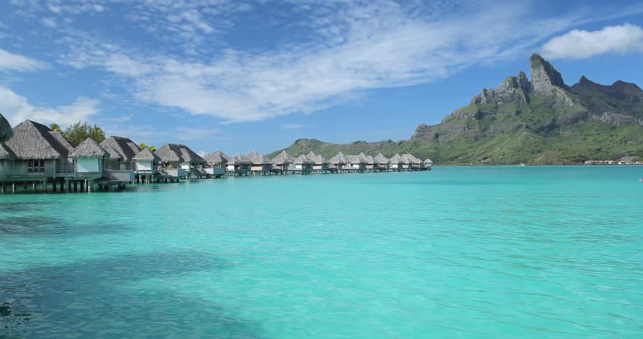 Houses built over clear blue water next to mountains