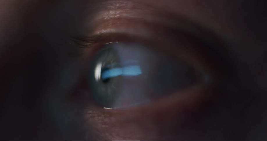 Extreme closeup of one graycolored eye in the dark with the reflection of two tvs showing static and interference