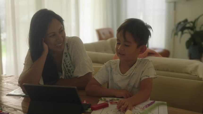 A mom and her son at home sitting at the table doing things on the computer maybe home schooling
