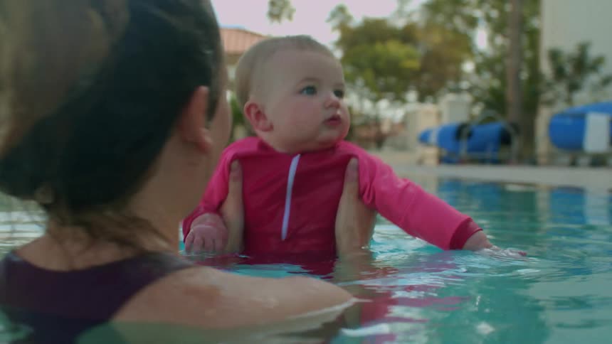 A mother holds her baby daughter in the water as they bob up and down in the pool