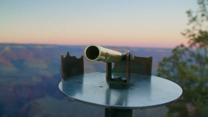 A telescope is sitting on a round table near a tree on high ground overlooking mountains