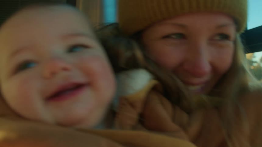 A mother holding her baby as they laugh and smile while in a vehicle