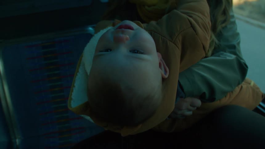 A mother holding her baby sitting in a vehicle while the baby leans back in the mothers arms