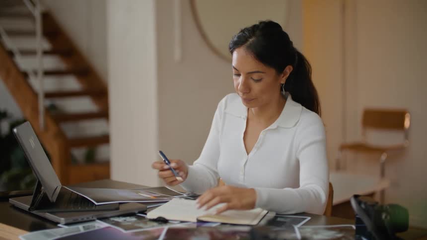 Woman with ponytail and white shirt works on documents and writes in notebook in room