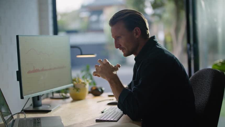 Man sitting at the office looks worried and pensive while working on computers