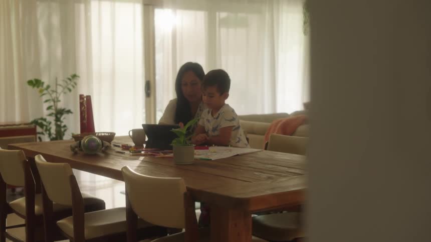 Mother and son sitting at the dining room table during the day with laptop and papers probably home schooling bonding