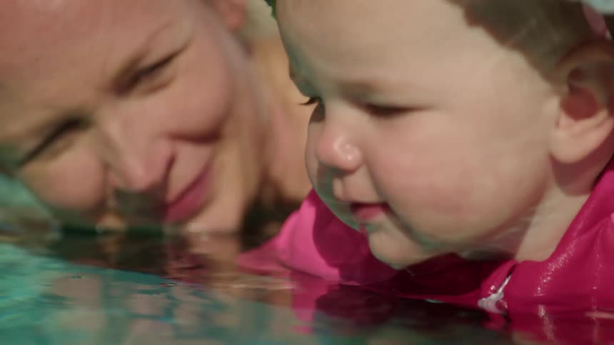 A woman shows her baby how to bubbles in pool water