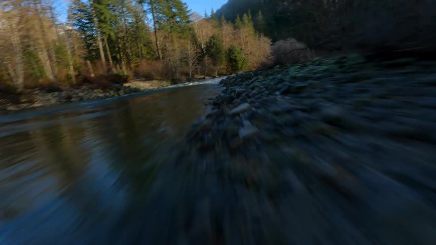 A dramatic FPV shot rushing over a river and then flying upwards to reveal a mountain