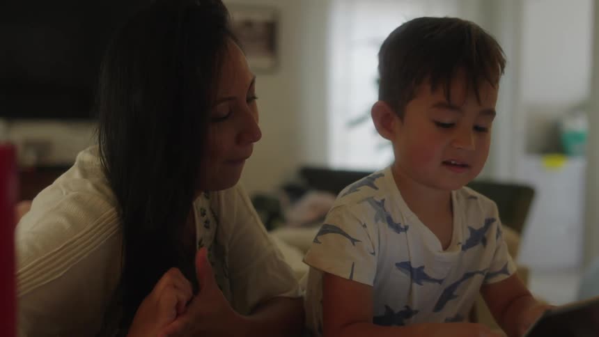 Mother and son uses tablet at table in the living room