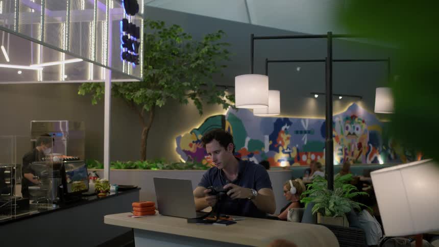 Businessman in blue shirt holds camera and uses laptop sitting at desk at the office