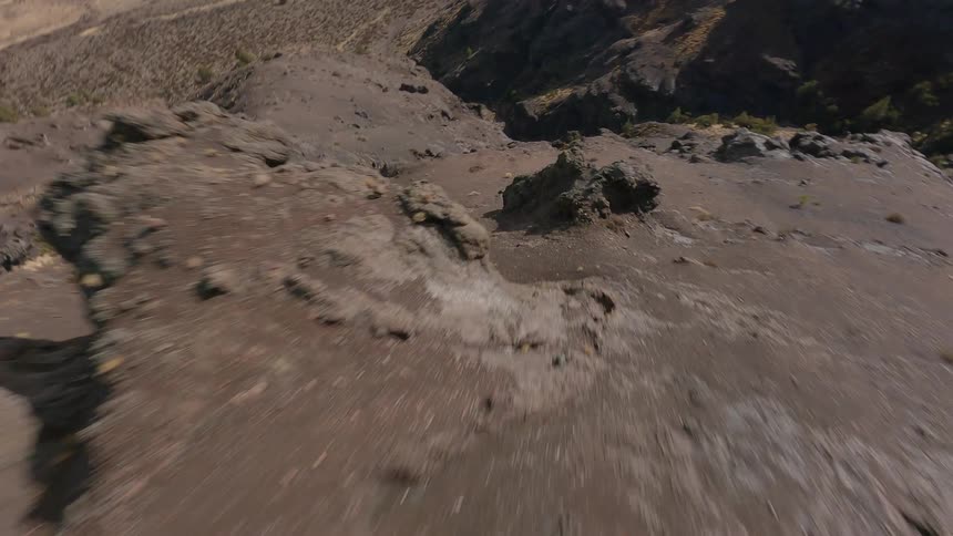 Dramatic FPV drone shot sweeping over trees on a dry and rocky mountain landscape that leads to plains stretching to the misty horizon