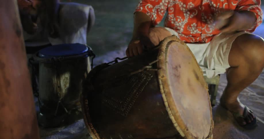 Two men beat on drums in the firelight
