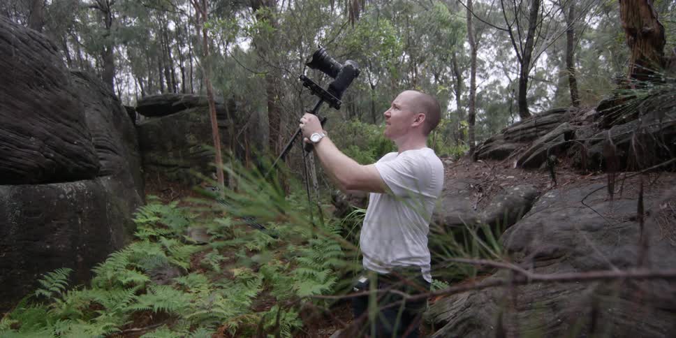 A man holds a camera on a tripod