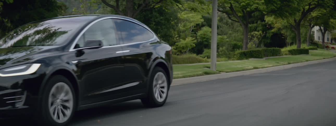 A black automobile is traveling on a neighborhood street