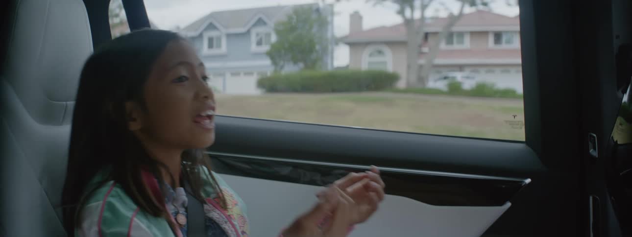 A young girl talks excitedly and plays with a bracelet while being driven in a car
