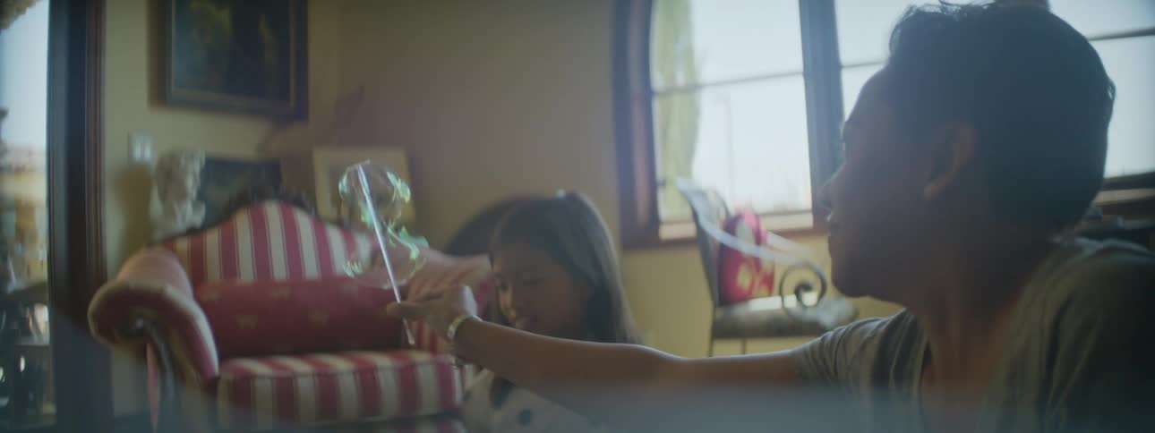 A mother and daughter play with a bubble wand in their home living room midday