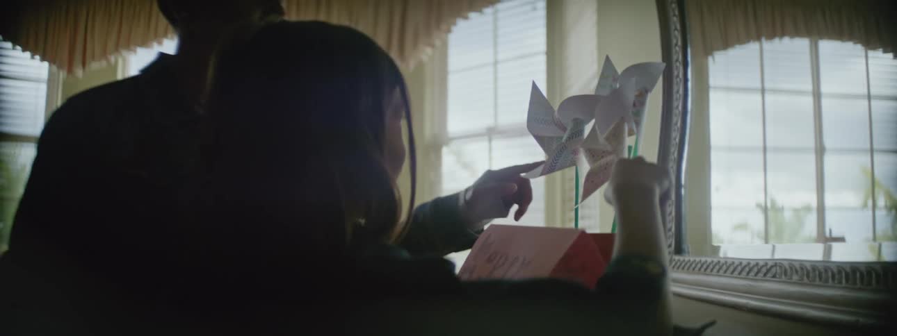 A mother and daughter walking up to a dresser with a card and handmade pinwheels on it