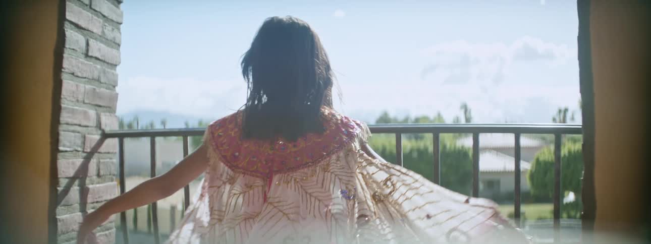 Girl opens her arms to extend a colorful translucent gauze cape in the balcony under the sun