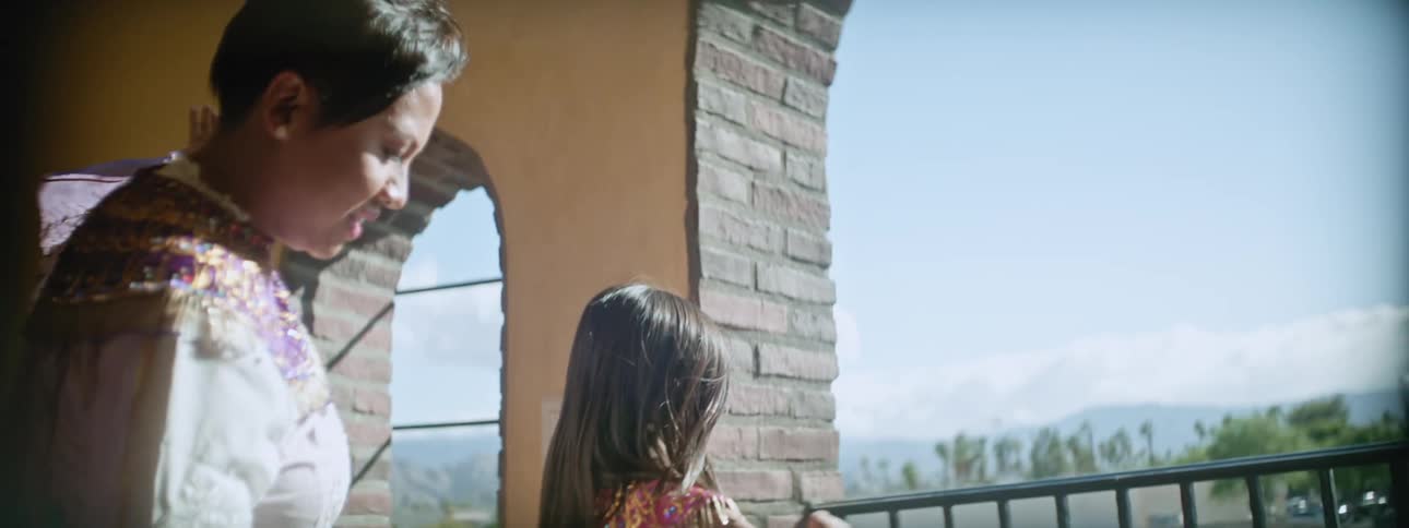 A mother dances with her daughter in a balcony doorway wearing dresses