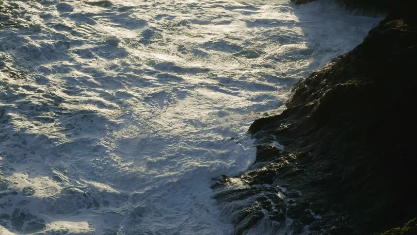Rough water waves splash against a cliff along the shore