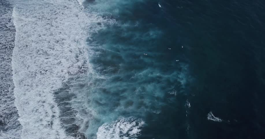 An overhead aerial view of foamy white waves crashing across an empty sea
