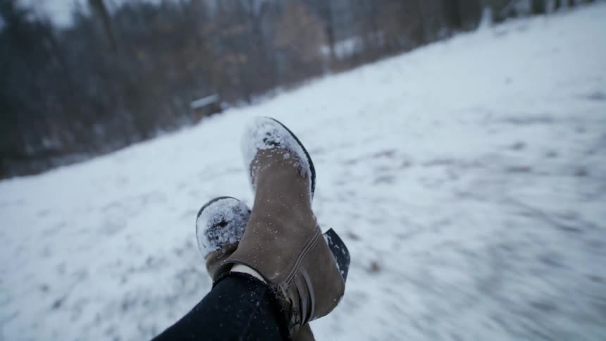 A persons feet with snow on their boots swinging back and forth over snowy grounds