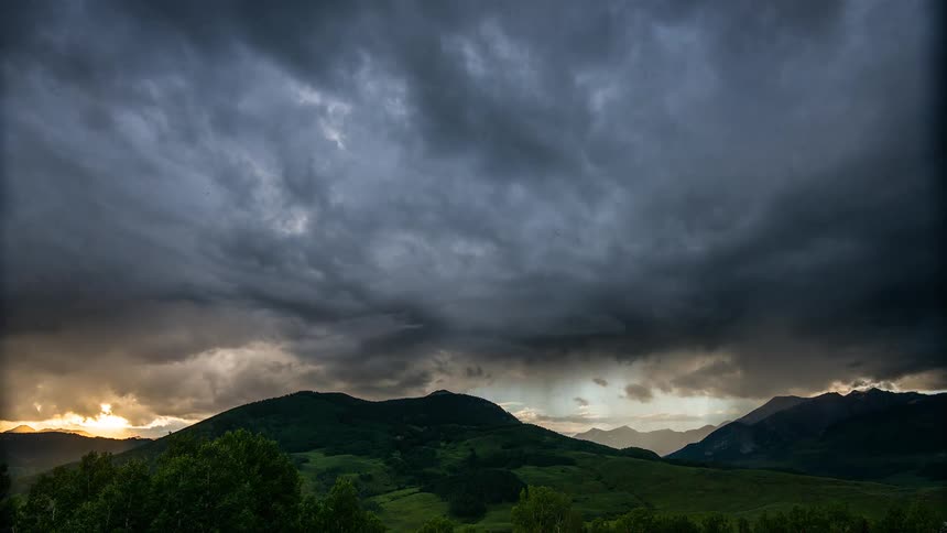 Dark clouds flow over mountains and forest before setting sun colors sky and clouds red